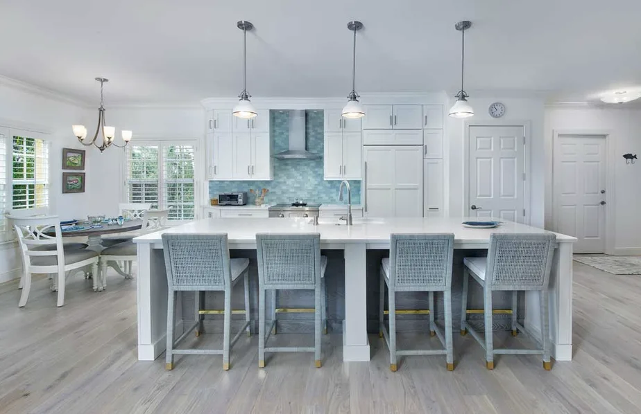 White kitchen with large white island, woven counter stools, blue glass tile backsplash and pendant lights