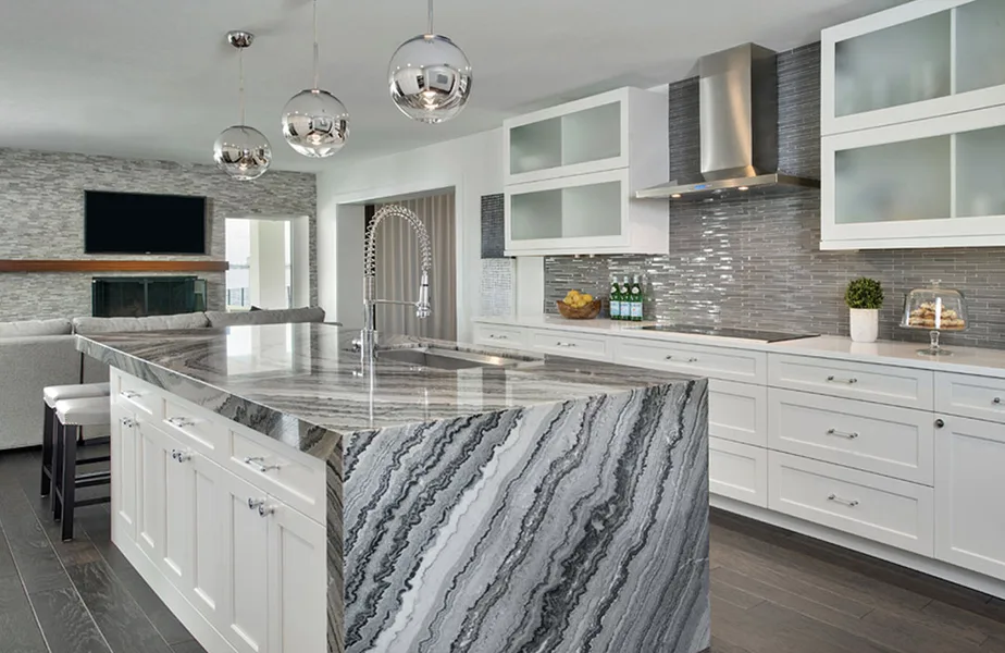Modern kitchen with white cabinets, gray veined waterfall stone island, glass tile backsplash and chrome pendants