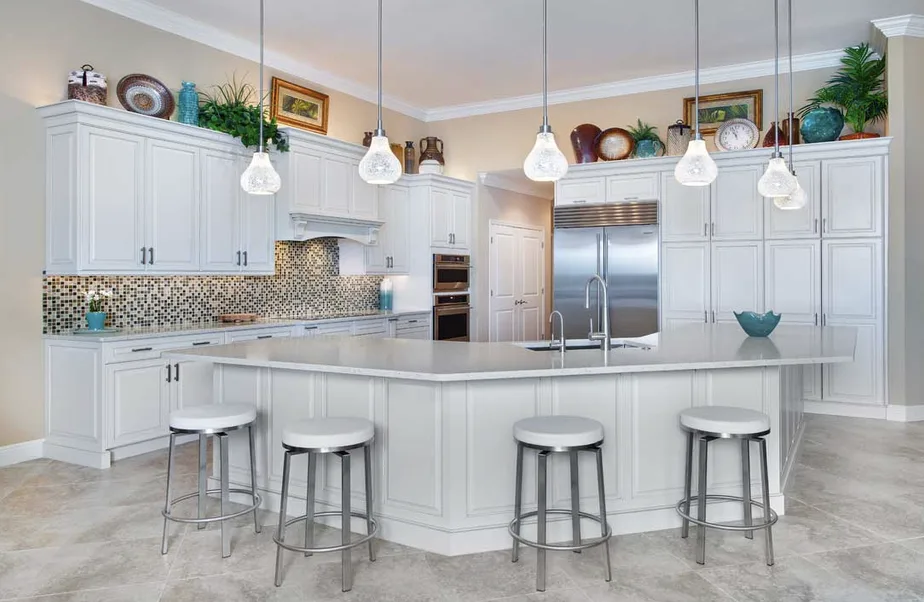 White kitchen with angled island, light countertop, mosaic tile backsplash, stainless refrigerator and glass pendants