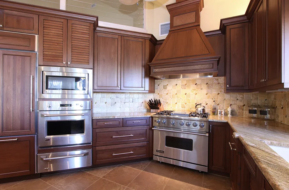 Wood kitchen cabinetry with wood range hood, stainless range and wall ovens, granite countertop and stone tile backsplash