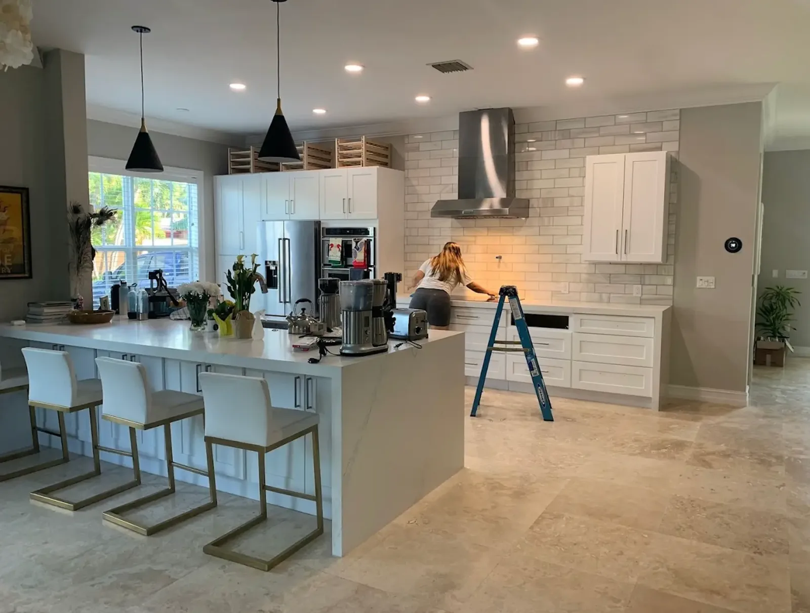 White shaker kitchen with waterfall quartz island and gray subway tile backsplash during finishing work, ladder on the floor