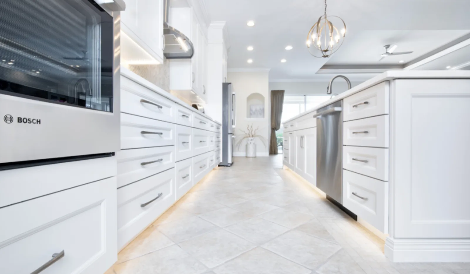 White kitchen cabinets and island with toe-kick lighting, stainless dishwasher and diagonal tile floor