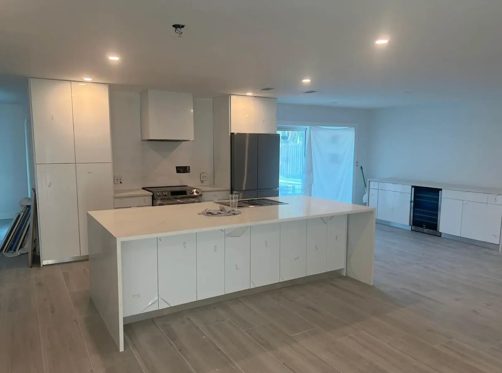Open kitchen with white gloss cabinets still in protective film, quartz waterfall island and recessed lighting before final trim