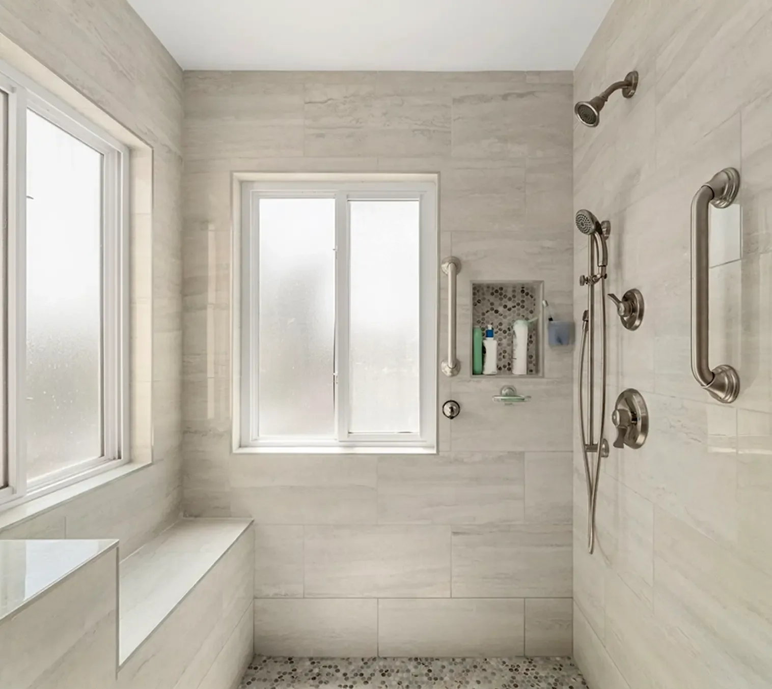 Large walk-in shower with beige large-format tile, built-in bench, tiled niche, pebble floor, handheld shower and grab bars