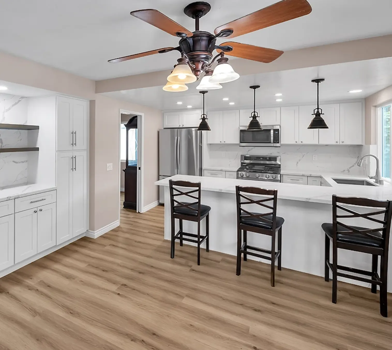 White shaker kitchen with marble-look quartz counters and backsplash, peninsula seating, black pendants, stainless appliances and wood-look flooring