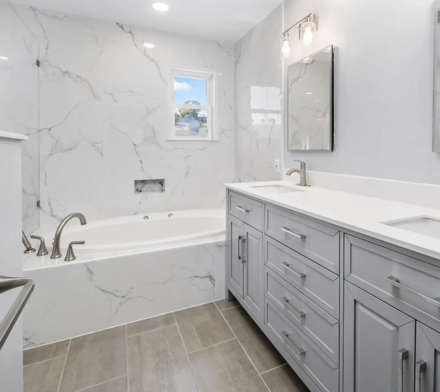 Bathroom with white marble-look large-format tile tub surround and shower, recessed niche, gray double vanity with white top and wood-look floor tile