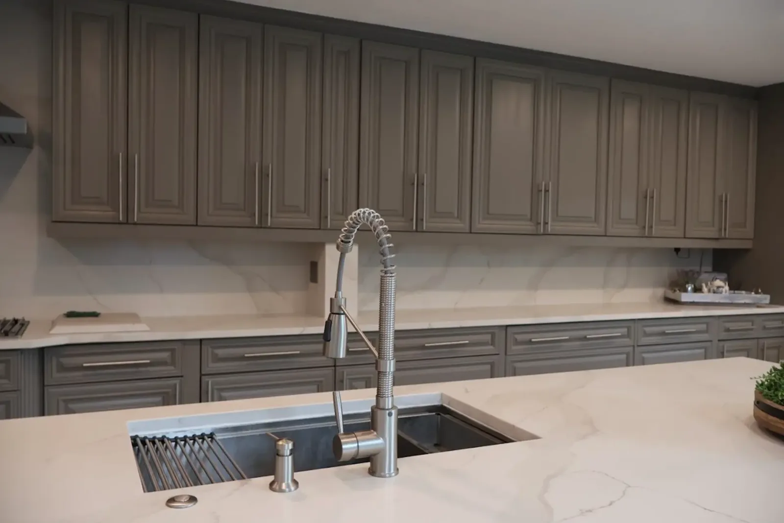 Gray raised-panel kitchen cabinets with full-height marble-look backsplash and quartz island with undermount workstation sink
