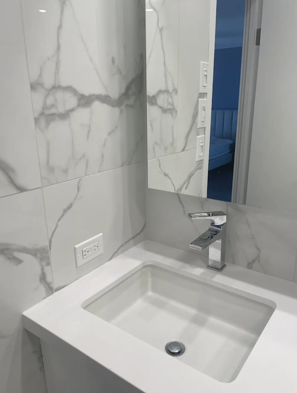 Bathroom with large-format marble-look wall tile, white vanity top, undermount sink and chrome faucet
